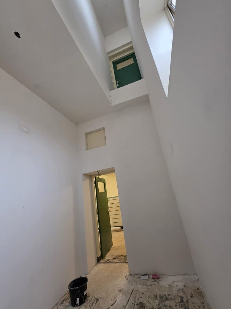 Hoge hal met groene deuren, strak gestuct